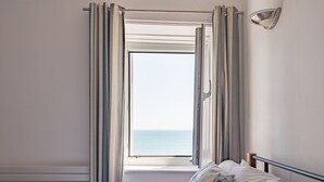A bedroom with a bed, a window with curtains, and a view of the sea. - Wave Cottage -  seaside cottage right on the beach by Bloom Stays (Sandgate)