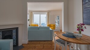 A living room with a sofa, yellow chairs, a dining table with plates, and a view through a doorway. - Wave Cottage -  seaside cottage right on the beach by Bloom Stays (Sandgate)