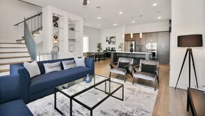 A spacious living room with a blue sofa, a glass coffee table, and a ceiling fan. - Private Rooftop - Amazing Skyline Views - Minute Maid Spacious - 3 Bd, 3.5 Ba (Houston)