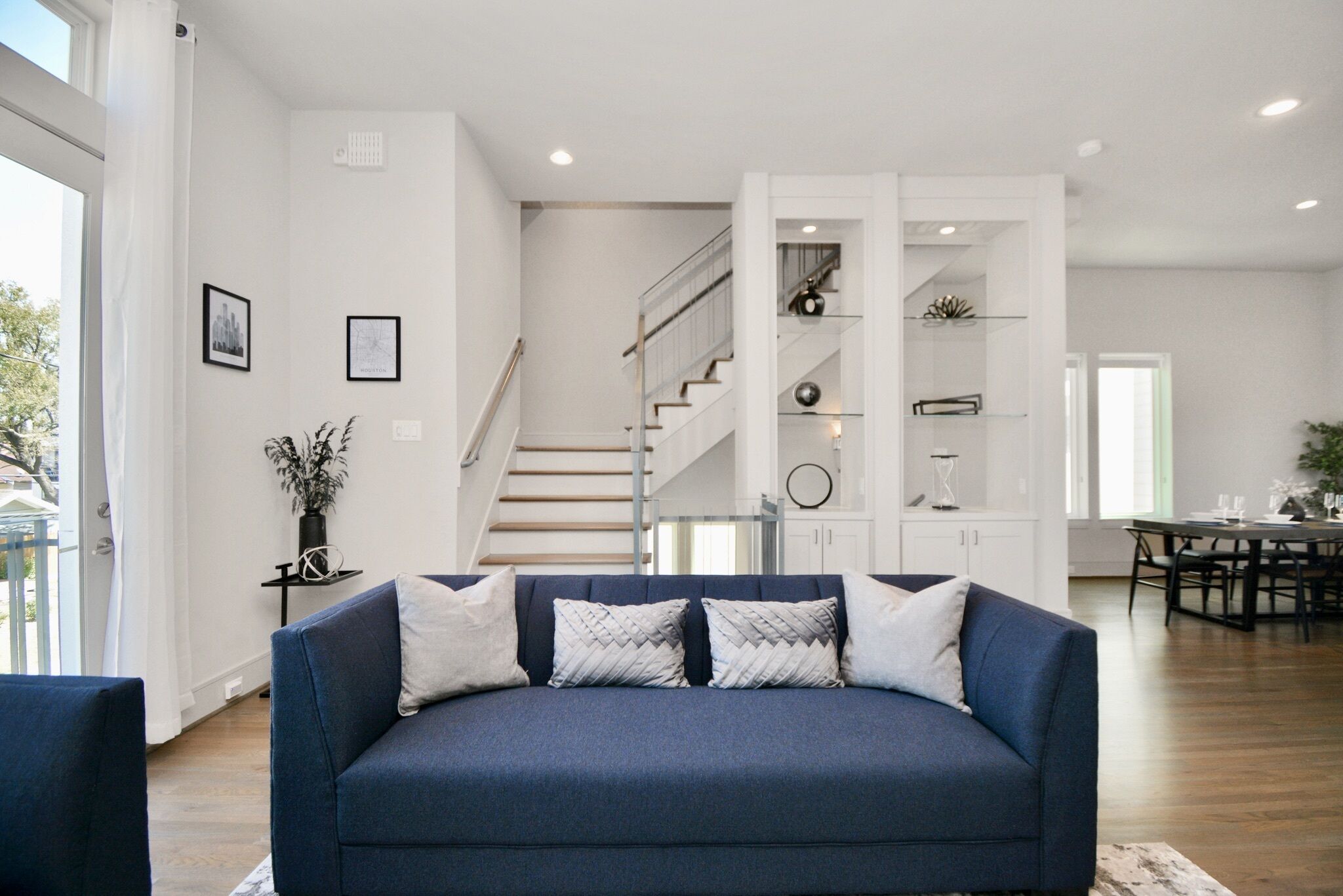 A modern living room with a blue sofa, a staircase, and a dining area.