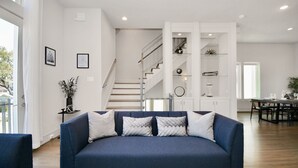A modern living room with a blue sofa, a staircase, and a dining area. - Private Rooftop - Amazing Skyline Views - Minute Maid Spacious - 3 Bd, 3.5 Ba (Houston)