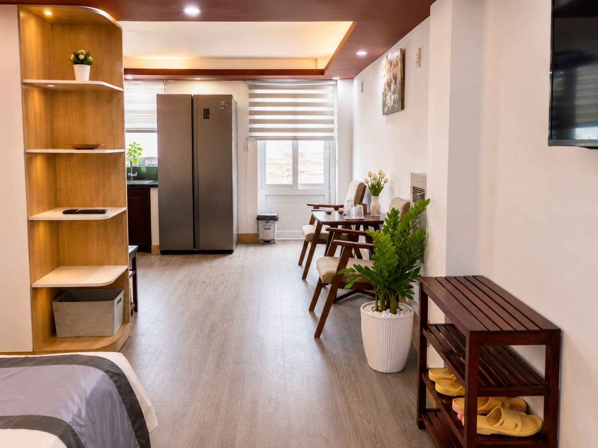 A modern hotel room with a bed, a dining area, a kitchen, and a large window.
