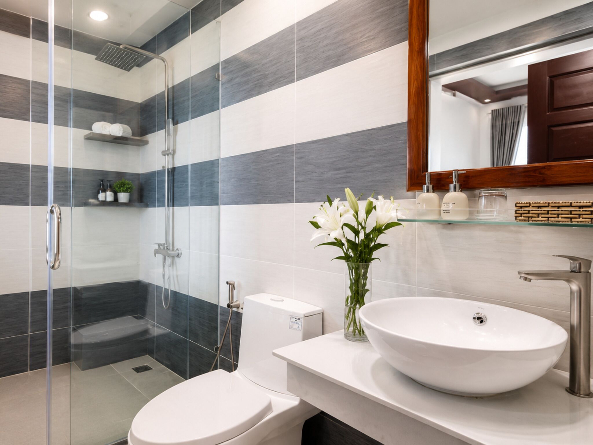 A modern bathroom with a glass shower enclosure, a white sink with a vessel basin, and a mirror above the sink.