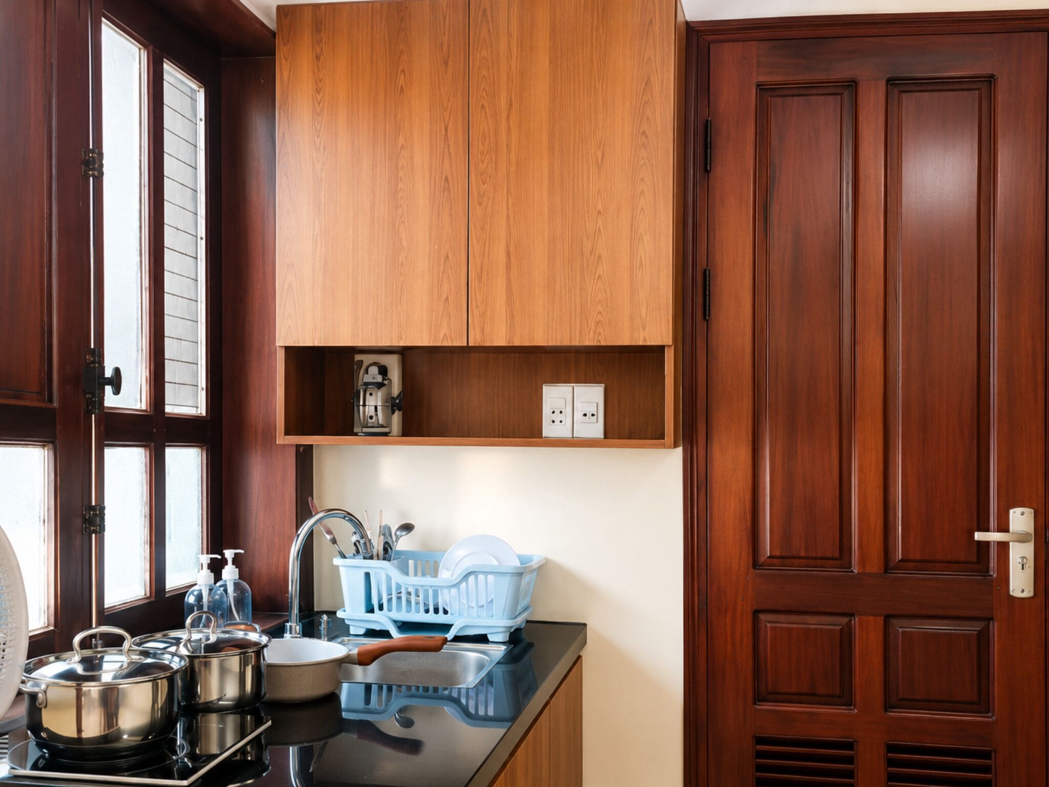 A kitchen with wooden cabinets, a sink, and a countertop with pots and a dish rack.