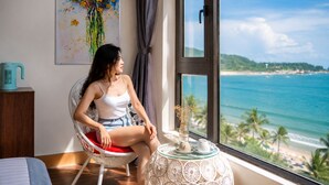 A room with a view of the ocean, a wicker chair, a small table with a vase, and a painting on the wall. - SONTRA SEA HOTEL (Da Nang)