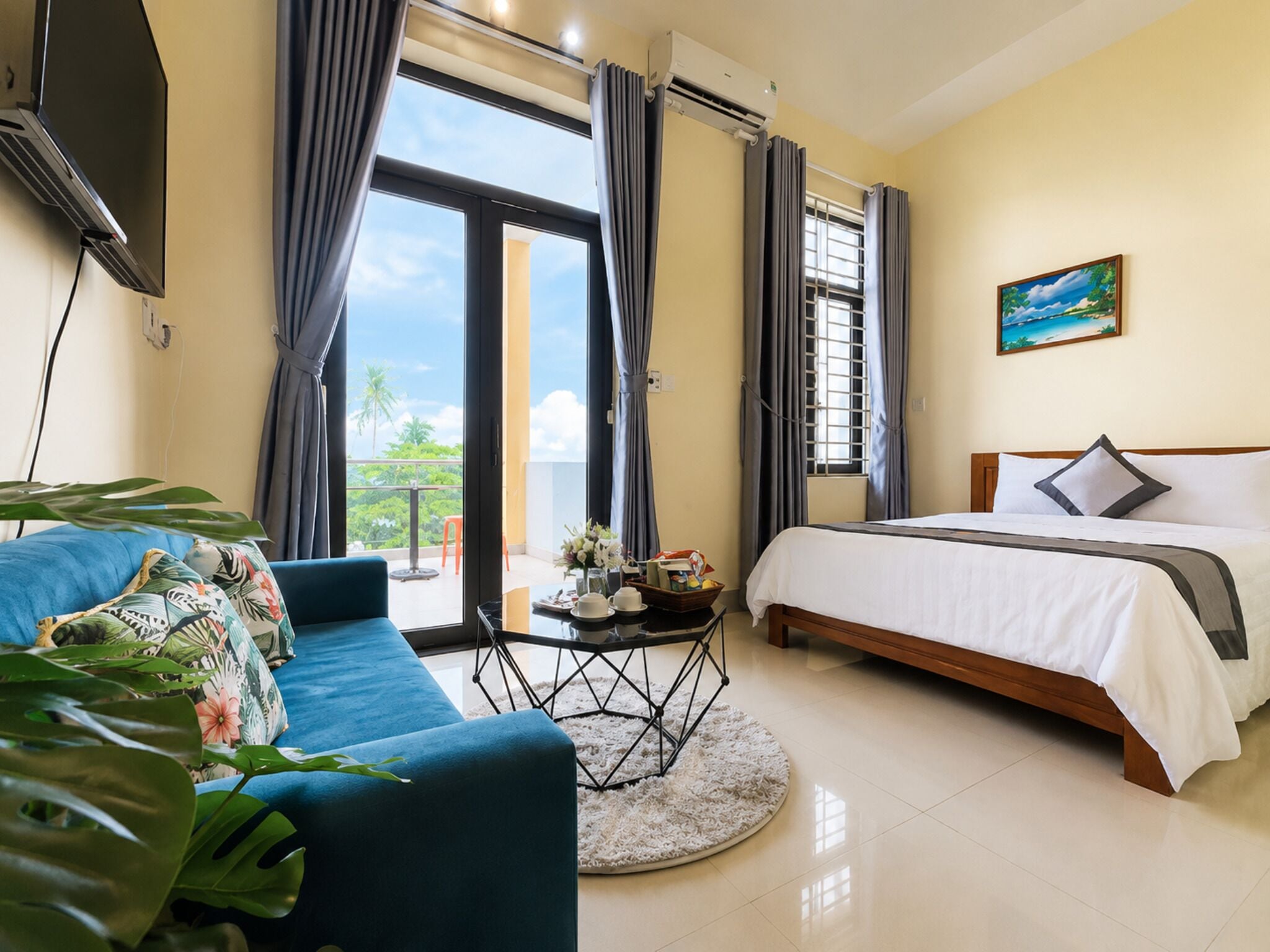 Habitación de hotel con cama, sofá, una mesita con un florero y vistas al exterior.