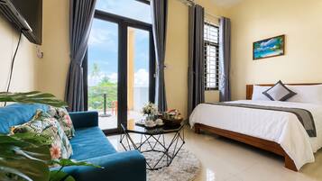 Habitación de hotel con cama, sofá, una mesita con un florero y vistas al exterior.