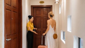 A hallway with a wooden door marked '103', a person in a yellow shirt, and another in a white dress with a suitcase. - SONTRA SEA HOTEL (Da Nang)
