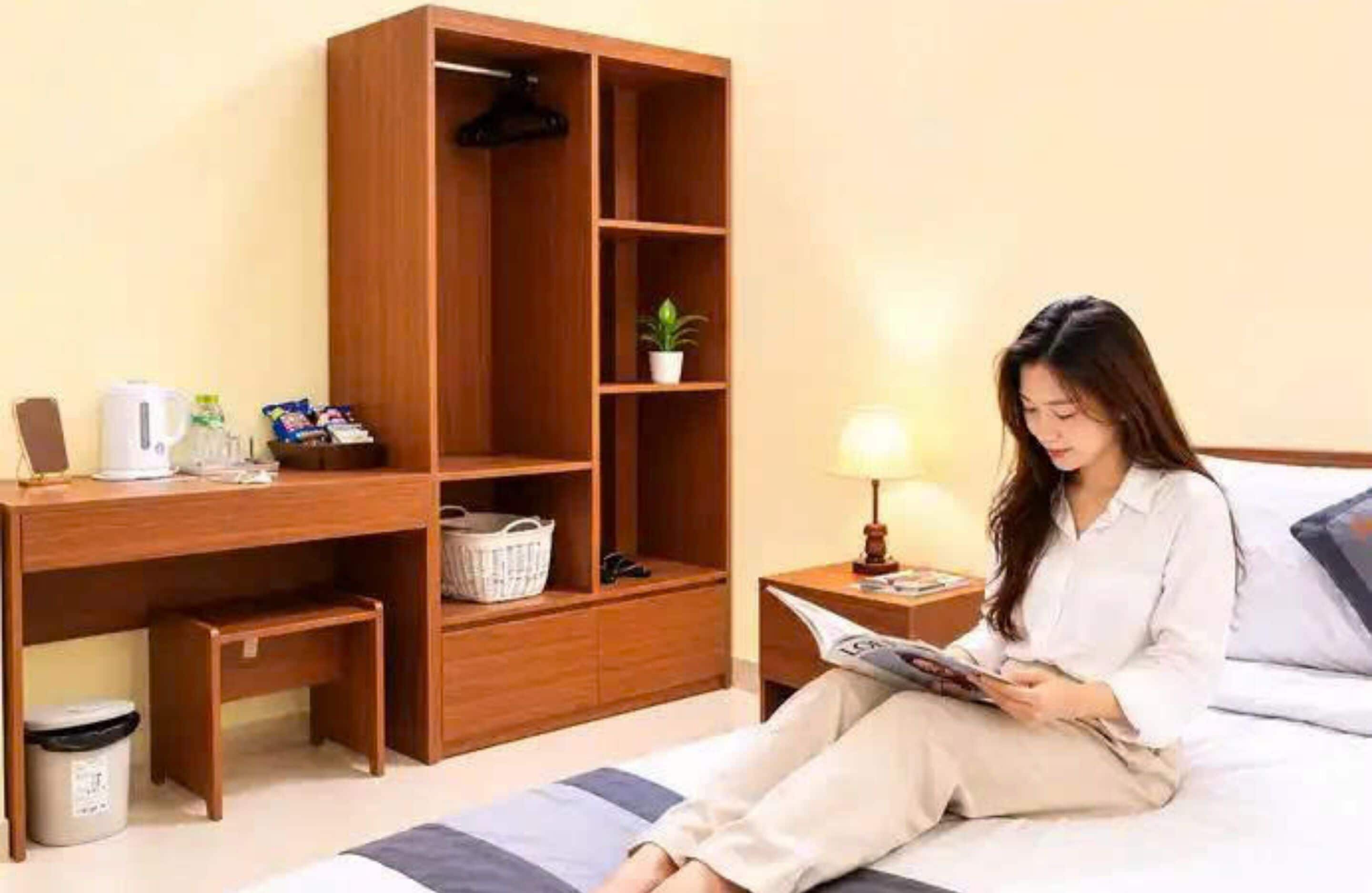 Una habitación con una cama, un escritorio de madera, una mesita de noche con una lámpara y una pequeña planta en maceta.