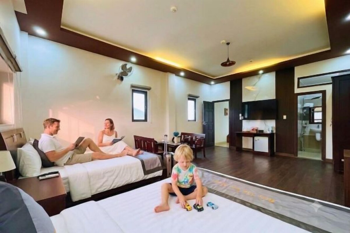 A hotel room with a large bed, a desk, and a chair. There is a child playing on the bed.