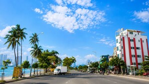 A coastal road with palm trees, a white building with red stripes, and a clear blue sky. - SONTRA SEA HOTEL (Da Nang)