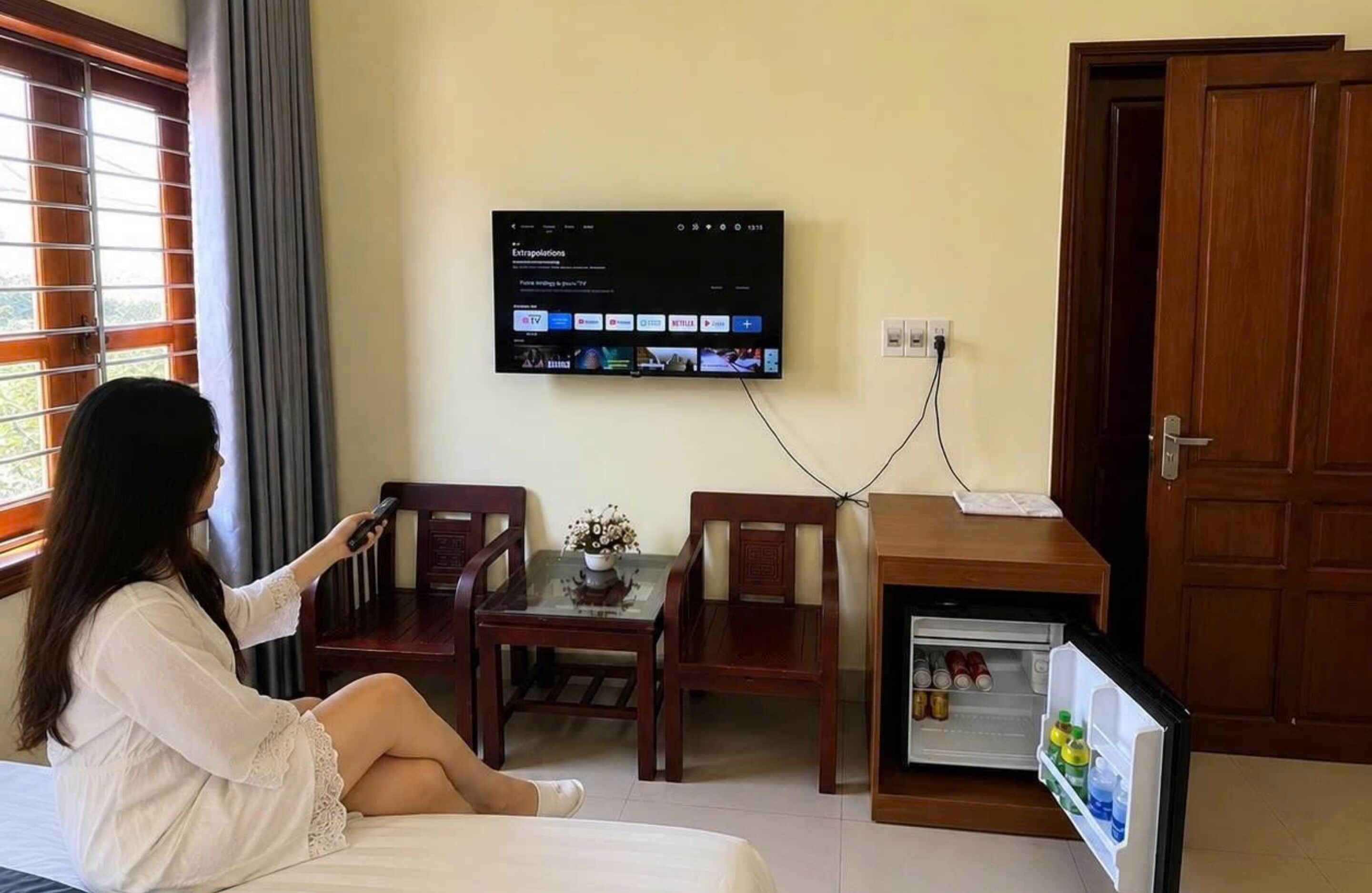 Une chambre d’hôtel avec un lit, un téléviseur fixé au mur, une petite table avec des chaises et une porte.