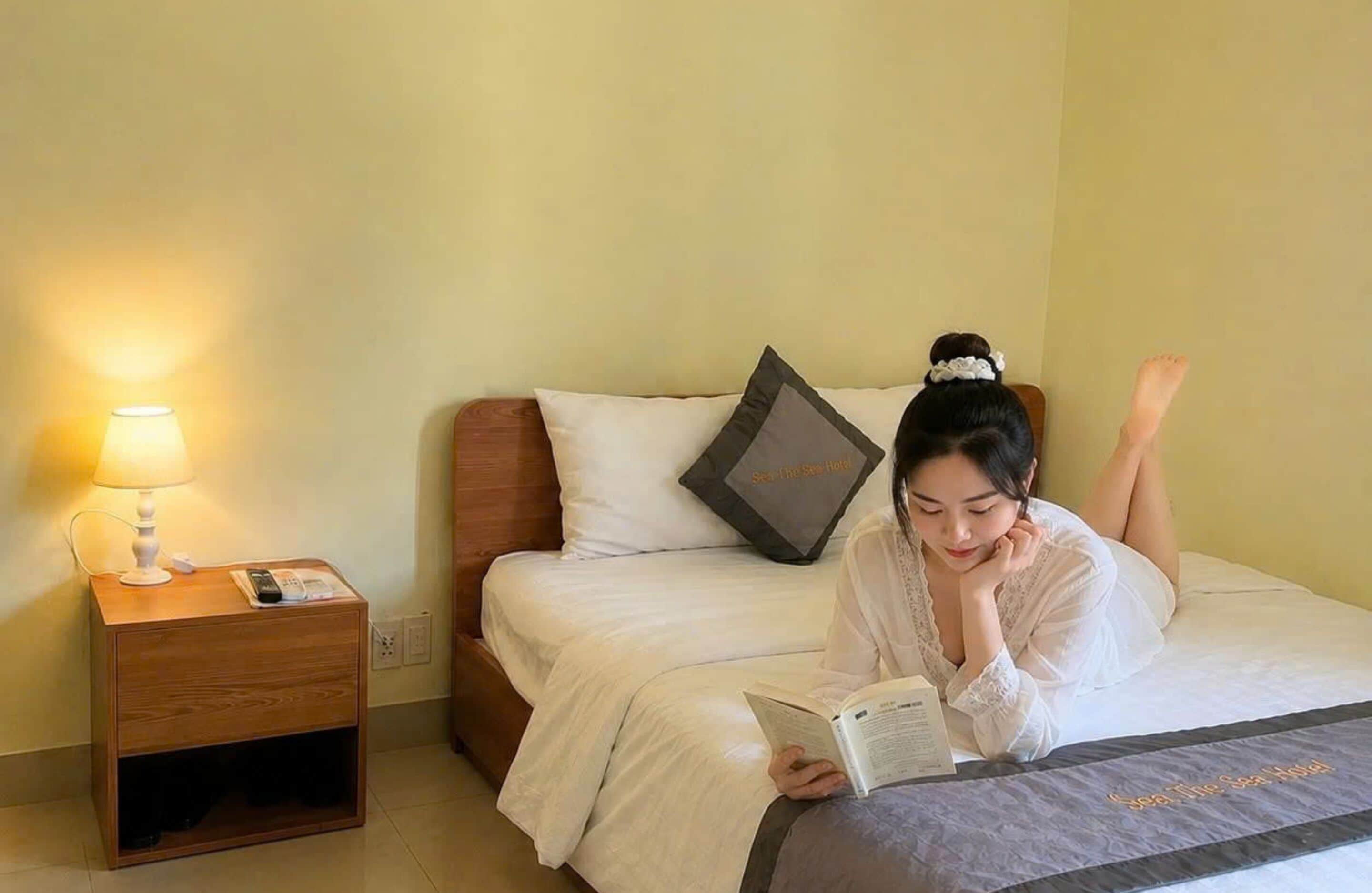 Una habitación de hotel con cama, una mesita de noche con lámpara y una almohada con el logotipo del hotel.