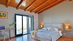 A bedroom with a bed, a desk with a laptop, a chair, and a large window.