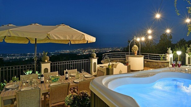 A rooftop terrace with a hot tub, dining table, chairs, and umbrellas.