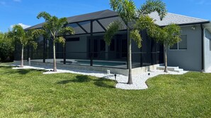 Une maison moderne dotée d’une piscine, entourée de palmiers et d’une pelouse bien entretenue.