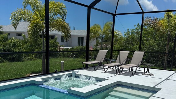 Une piscine avec un jacuzzi, entourée d’un patio couvert équipé de chaises longues.