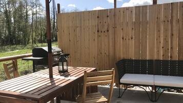 Eine Terrasse im Freien mit einem Holztisch und Stühlen, einem Grill und einer Laterne.