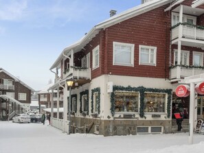 A building with a shop on the ground floor, a balcony with railings, and a snow-covered street.