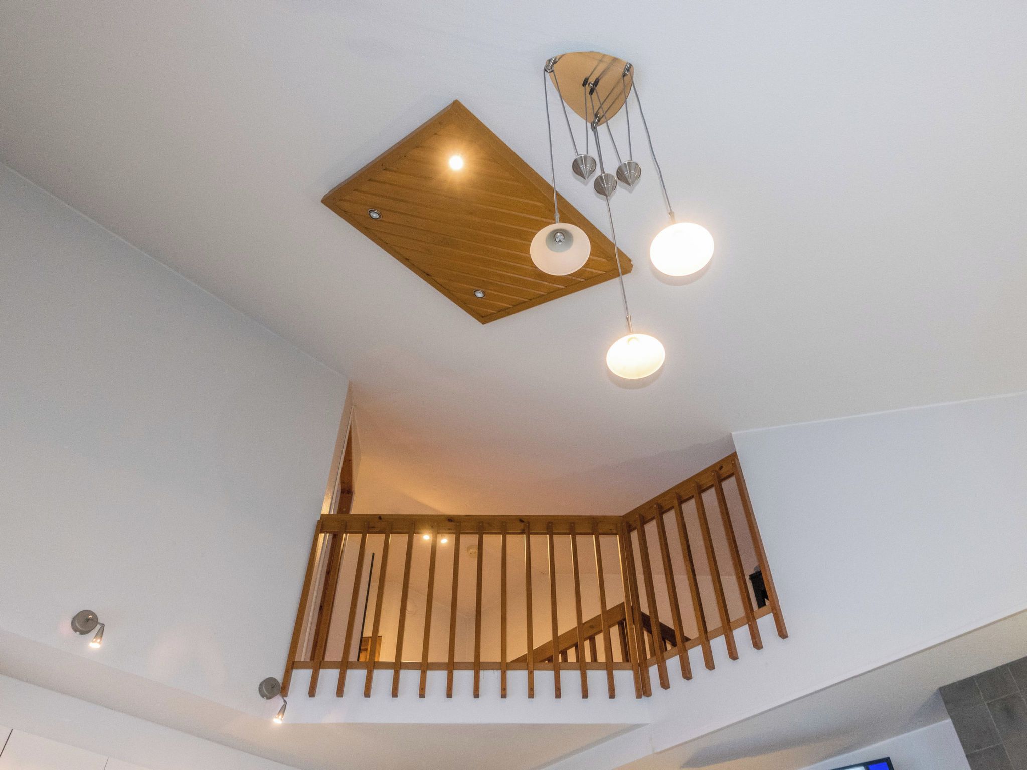Et moderne interiør med træloft, trappe med gelænder og hængende lamper.