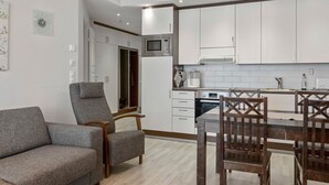 A modern kitchen with white cabinets, a dining table with wooden chairs, and a grey sofa.