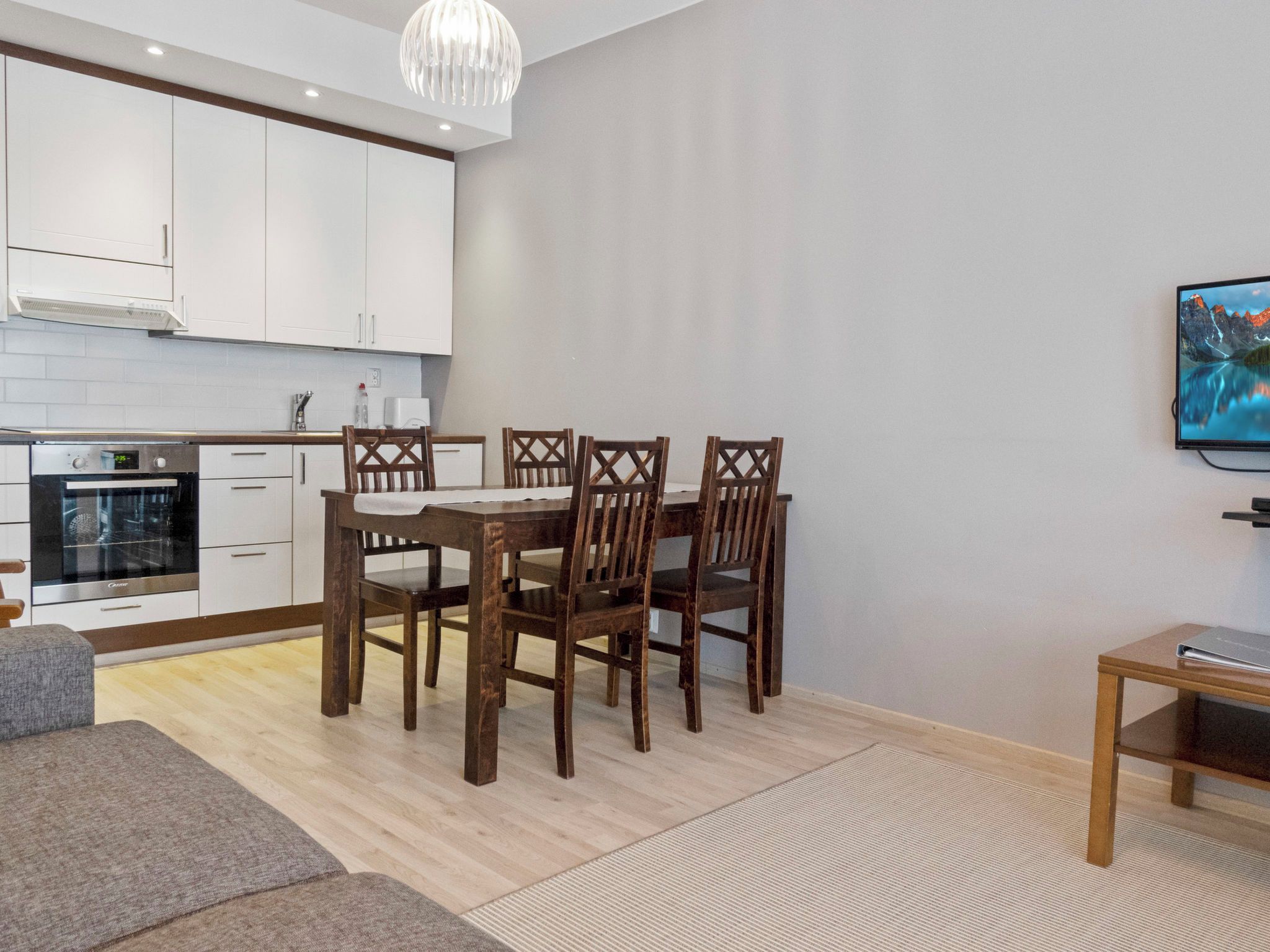 Una cocina moderna con armarios blancos, horno empotrado y comedor con mesa y sillas de madera.
