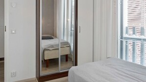 A bedroom with a bed, a wardrobe with a mirror, and a window with blinds.