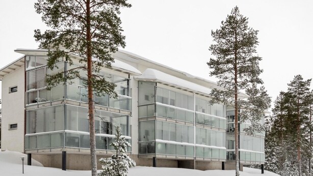 A modern building with large glass windows and a flat roof, surrounded by snow-covered trees.