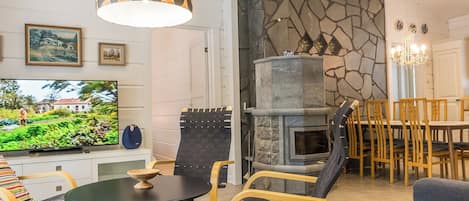 Un salon moderne avec une cheminée en pierre, un téléviseur et un coin repas doté de chaises en bois.