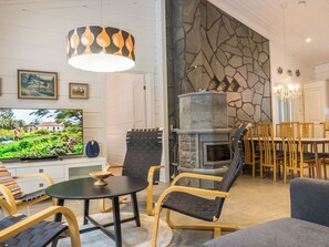 A modern living room with a stone fireplace, a television, and a dining area with wooden chairs.