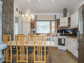 A modern kitchen with white cabinetry, a dining table with chairs, a chandelier, and a stone accent wall. - Petsukantähti by Interhome (Kittilä)