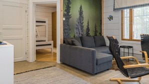 Une pièce chaleureuse avec un canapé gris, une chaise en bois, un lit superposé et une fresque représentant des arbres.