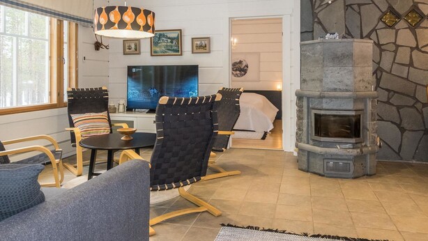 Un salon chaleureux avec une cheminée en pierre, des fauteuils confortables, un téléviseur et des œuvres d’art accrochées aux murs.