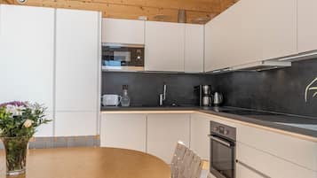 A modern kitchen with white cabinets, a black countertop, a stainless steel range hood, and a round wooden table with a chair.