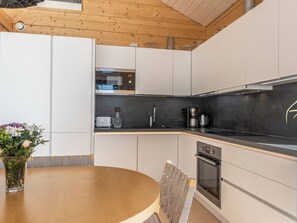 A modern kitchen with white cabinets, a black countertop, a stainless steel range hood, and a round wooden table with a chair. - Paloranta by Interhome (Kuhmo)