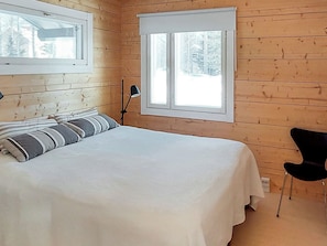 Un dormitorio con una cama, una silla, un ventanal y una lámpara.