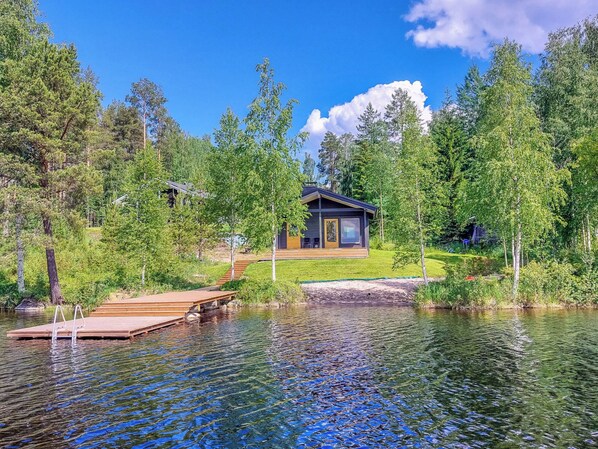 A lakeside cabin with a dock, surrounded by trees and a clear sky.