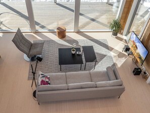 A modern living room with a grey sofa, two black coffee tables, a floor lamp, and a television on a wooden wall. - Paloranta by Interhome (Kuhmo)