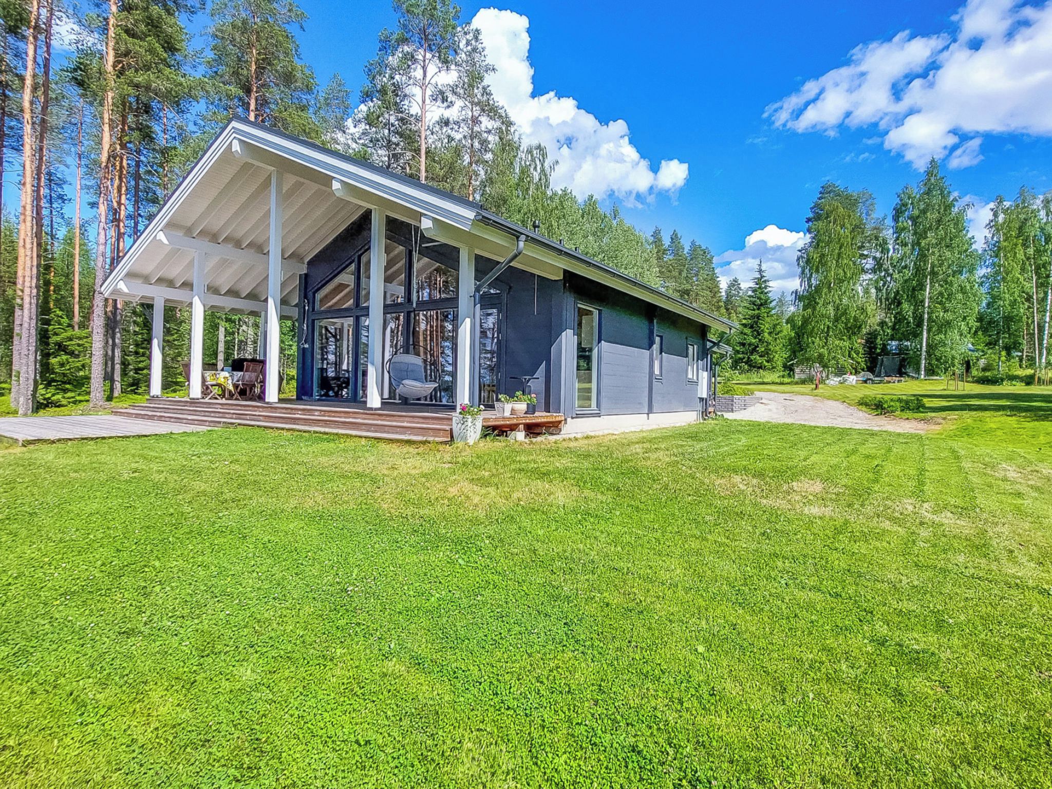 Een modern huis met een overdekte veranda, omringd door een verzorgd gazon en hoge bomen.