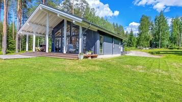 Een modern huis met een overdekte veranda, omringd door een verzorgd gazon en hoge bomen.