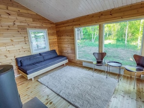 Un interior de madera con un sofá, un tapete y dos sillones cerca de amplias ventanas.