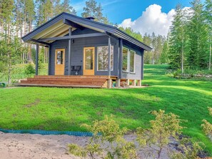 A two-story cabin with a wooden deck, large windows, and a surrounding grassy landscape. - Paloranta by Interhome (Kuhmo)