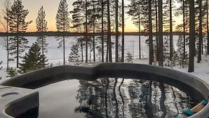 Un jacuzzi rodeado de nieve y árboles, con un atardecer al fondo.