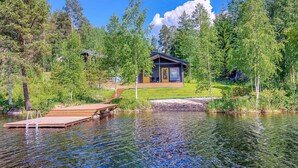 Una cabaña junto a un lago con un muelle de madera, rodeada de árboles.
