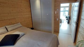 Een slaapkamer met een bed, een kledingkast en uitzicht op een besneeerd landschap door een geopende deur.