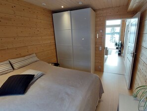Een slaapkamer met een bed, een kledingkast en uitzicht op een besneeerd landschap door een geopende deur.