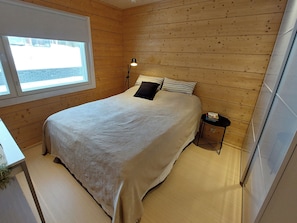 Quarto com cama, mesa de cabeceira, abajur e janela.