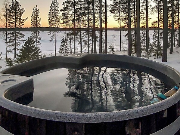 A hot tub surrounded by snow-covered ground and trees, with a sunset in the background.