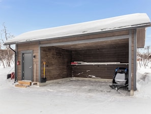 Un garaje techado con interior de madera, techo cubierto de nieve y suelo nevado.