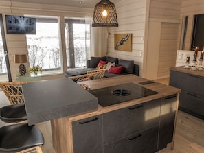 Et moderne køkken med en central ø, indbyggede skabe og et spiseområde med sofa og stole.